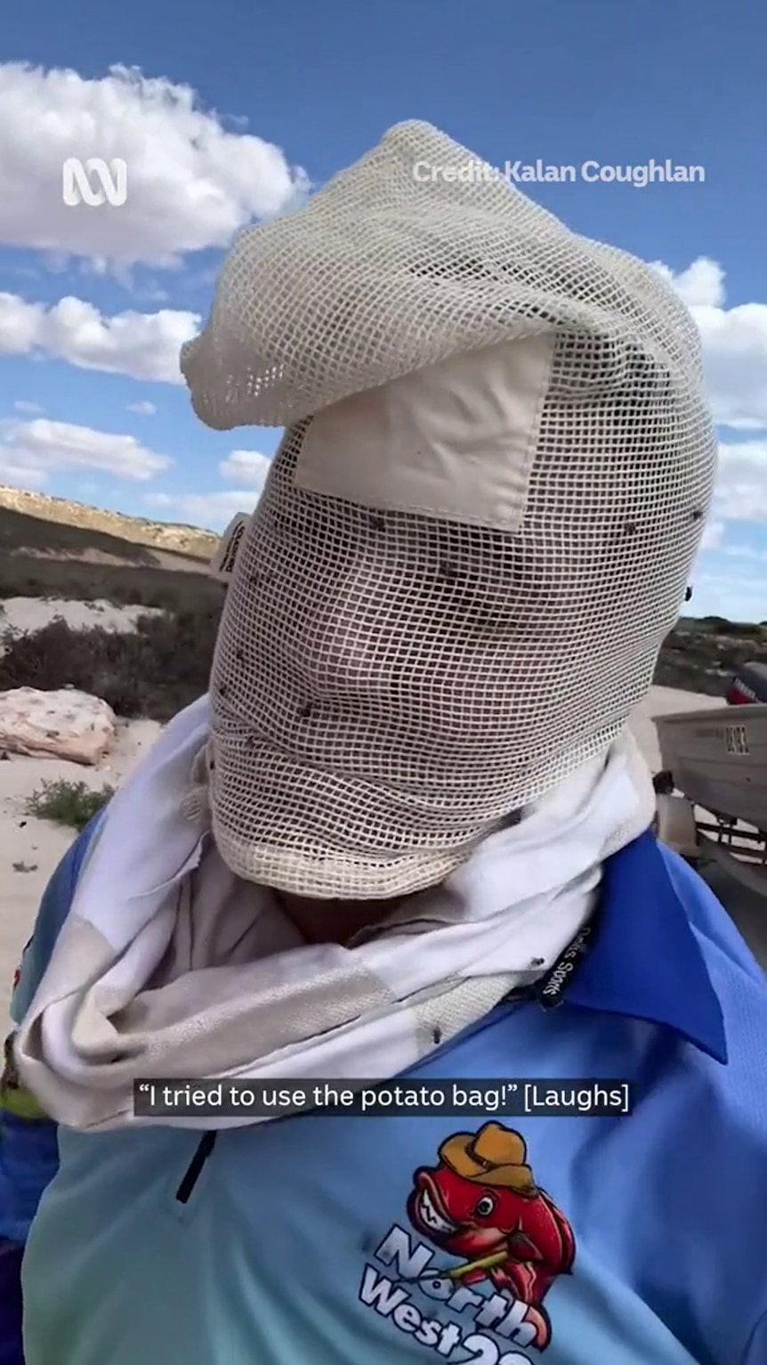 A person dressed in a blue shirt has their face concealed by fly-covered  white netting stretched over their head