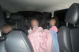 Three children in a car in their child restraints with faces blurred, dark outside