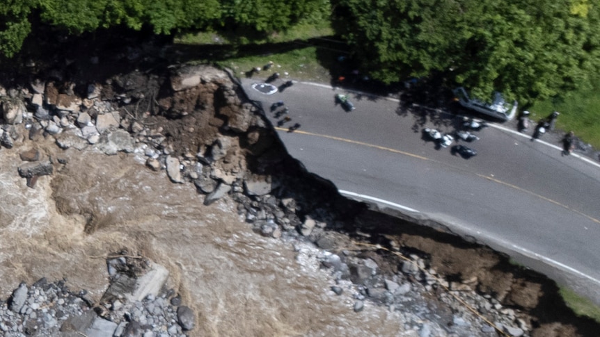 An aerial shot shows a road split in two as water rushes through where the road used to be,