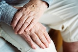 An elderly man crosses his hands.