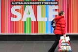 A woman walks past a store displaying a sale sign.