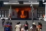 A crowd near a building's front door, which is burning.
