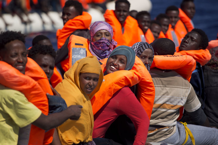 Image: Migrant women smile on board of a dinghy as they sail in the Mediterranean sea