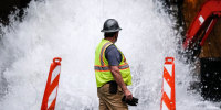 Image: A crew member walks near a broken water transmission line