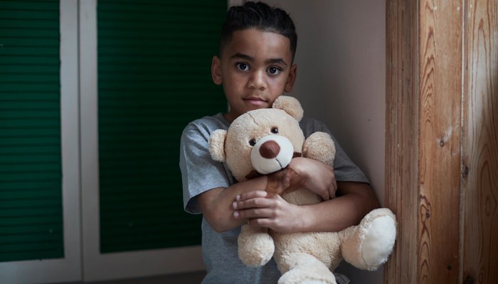 Boy looking into the camera holding a teddy bear