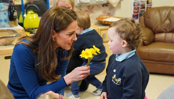 Kate Middleton kneeling down to hand flower to child at Ballymena Sure Start Childrens Centre