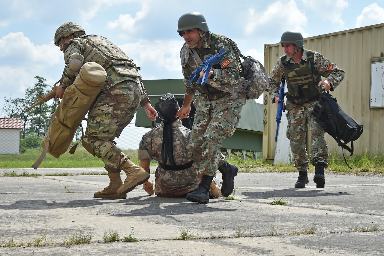 Soldiers drag a casualty training dummy away from a containerized building during training.