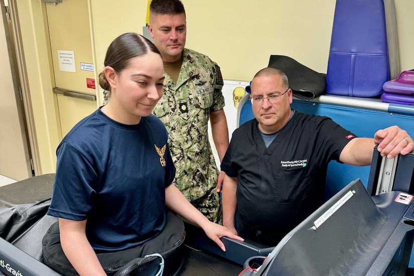 A sailor uses an anti-gravity treadmill as another service member and a physician watch.