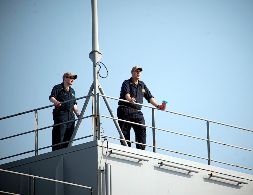 Two sailors stand aboard a ship.