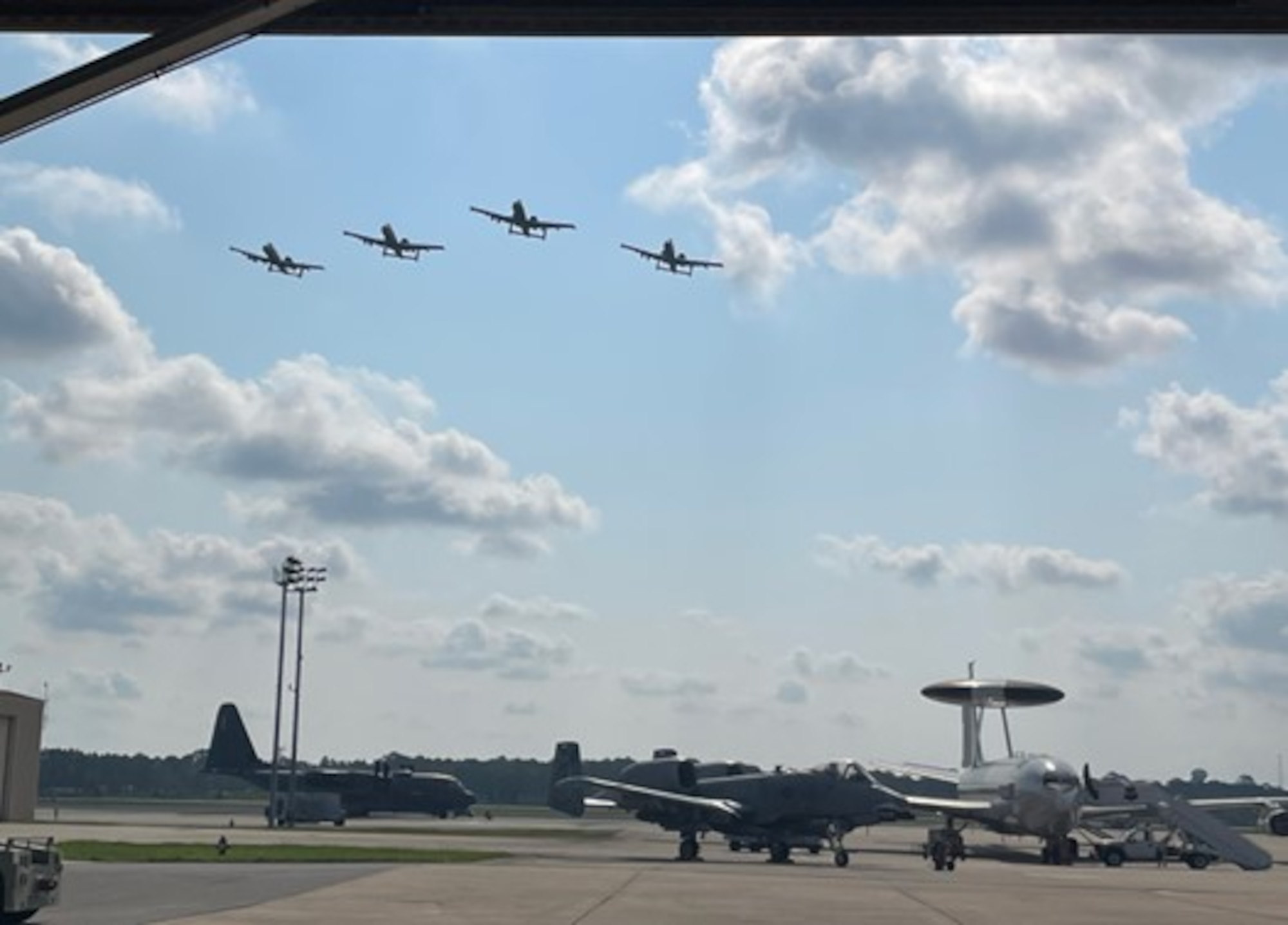 photo of four A-10Cs flying over an airborne warning and control system aircraft and two A-10Cs on the flight line.
