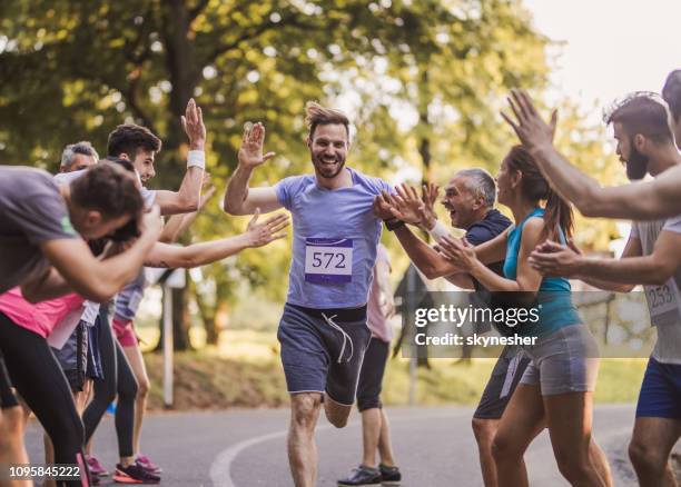cheerful marathon runner greeting group of athletes at finish line. - track event stock pictures, royalty-free photos & images