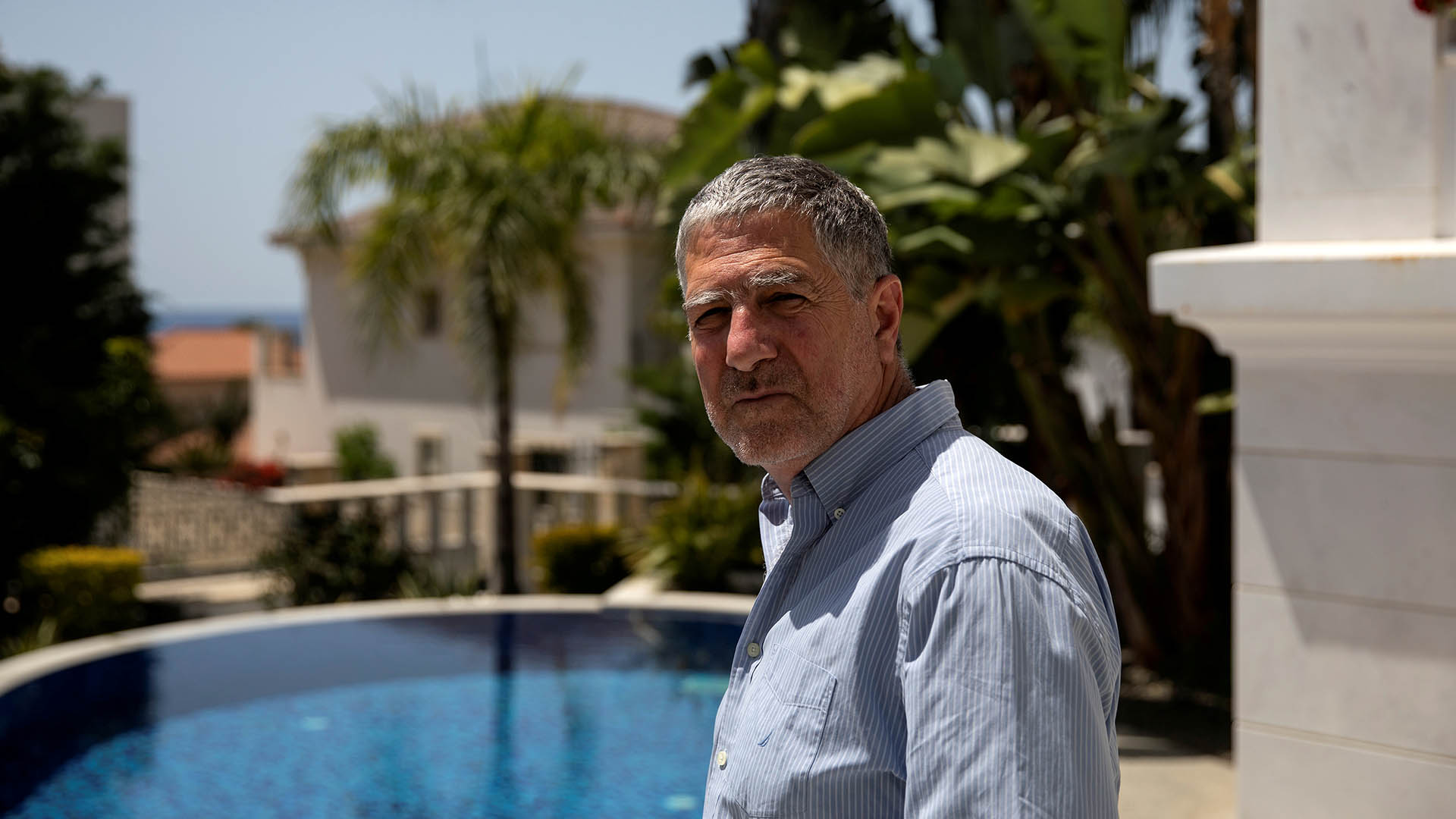 Grey-haired man in blue shirt standing in front of a swimming pool