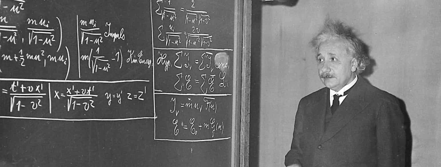 Mann med bart som står og ser på en tavle der det er skrevet mange matematiske formler