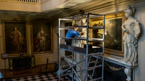 Cleaning the figure of Mars on the chimneypiece in the Great Hall at Ham House, Surrey with paintings in the background.