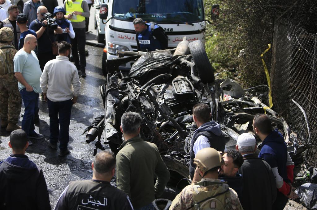 People and Lebanese army soldiers stand around a wrecked car targeted by an Israeli drone