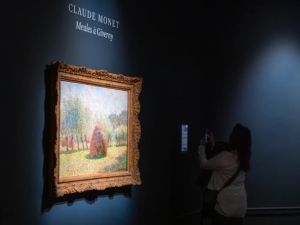 A person looks at a large framed impressionist painting in a dark room