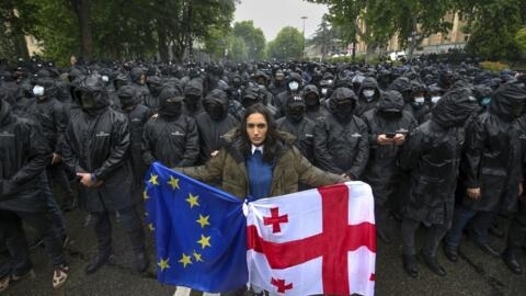 A woman holds a Georgian national and an EU flags in front of riot police during an opposition protest against "the Russian law" near the parliament in Tbilisi, Georgia, on May 14, 2024.