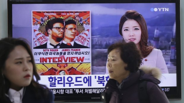 People walk past a TV screen showing a poster of Sony Picture's <i>The Interview</i> in a news report at the Seoul Railway Station in South Korea.