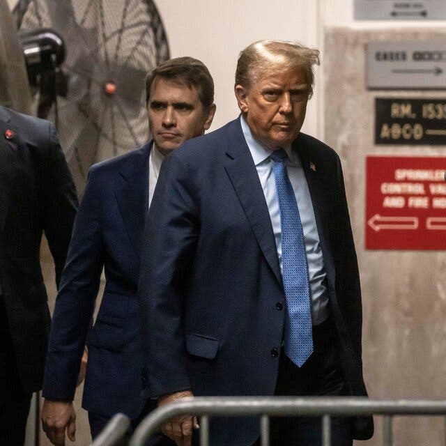 Donald Trump walks outside a courtroom, trailed by several men.