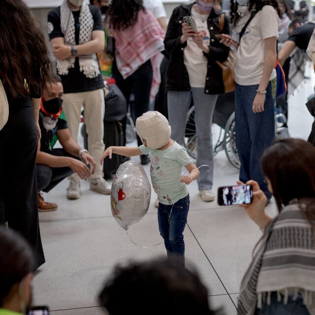 A child whose head is bandaged all over plays with a balloon among a crowd of people.